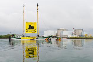 Das Greenpeace-Schiff Beluga II fährt vor dem französischen Atomkraftwerk Fessenheim vorbei. Zwischen den beiden Masten und den Aktivist:innen im Schlauchboot weht ein Banner mit der Botschaft "Europa nicht länger auf's Spiel setzen!". Ein zweiter Banner zeigt die Botschaft in französischer Sprache: "Schaltet alternde Kraftwerke ab!"
