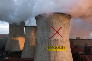 Luftaufnahme eines Greenpeace-Protests auf einem Kühlturm des RWE-Kraftwerks Neurath. Die Aktivist:innen haben ein großes "X" auf den Kühlturm gemalt und darunter ein Transparent mit der Aufschrift "Shutdown" angebracht. 