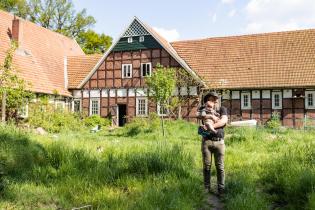 Björn Scherhorn hält sein jüngstes Kind vor seinem Hof