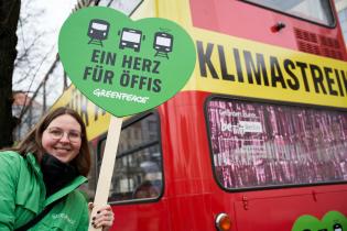 Aktivistin mit Schild "Ein Herz für Öffis" vor rotem Bus