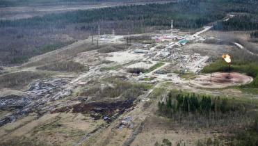 Luftaufnahme der Rosneft-Ölförderanlage, drumherum abgeholzter Wald und Öllachen. Aus einem Schornstein züngelt eine Gasflamme.
