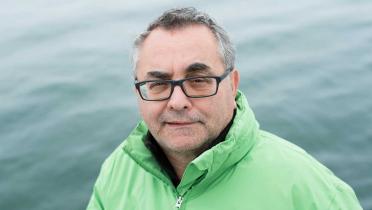 Porträtfoto von Jürgen Knirsch, Greenpeace-Experte für Handel. Er trägt eine grüne Jacke, im Hintergrund ist Meer zu sehen