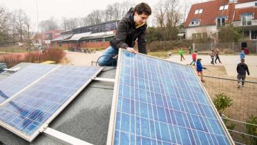 Auf dem Dach der Stadtteilschule Blankenese kniet ein Schüler. Er installiert ein Solar-Panel. Im Hintergrund ist der Schulhof zu sehen, auf dem ein halbes Dutzend Kinder spielt.