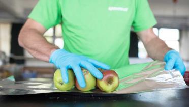 Ein Greenpeace-Mitarbeiter im grünen Shirt verpackt einige Äpfel in Alufolie.