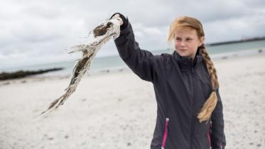 Ein Mädchen hält ein Stück Müll, das es am Strand der Helgoländer Düne aufgesammelt hat