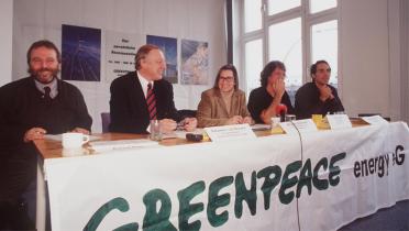 Fünf Personen sitzen an einem Tisch, an dem ein Banner mit der Aufschrift "Greenpeace Energy eG" hängt