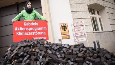 Eine AKtivisten steht mit einem Banner auf dem Kohlehaufen, Aufschrift: "Gabriels Aktionsprogramm Klimazerstörung"