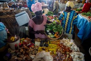 Ein Frau an einem afrikanischen Marktstand voller verschiedener Produkte