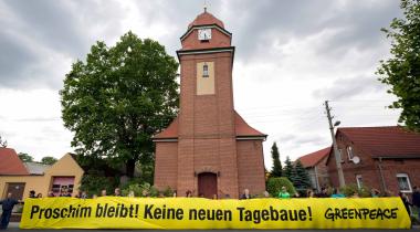 Großes gelbes Protestbanner sagt "Proschim bleibt! Keine neuen Tagebaue!"vor der Kirche in Proschim.
