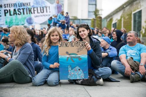 Menschen demonstrieren mit Greenpeace gegen die Plastikflut und für eine umweltfreundliche Konsumwende. Kinder und Jugendliche unterstützen mit selbstgemalten Schildern den Protest,