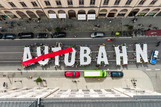 Foto von oben auf Menschen, die Buchstaben hochhalten: AUTOBAHN - das Wort Auto ist durchgestrichen
