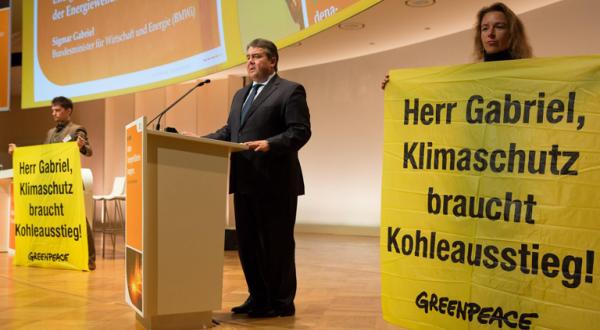 Gabriel bei einer Rede, auf beiden Seiten stehen Greenpeace-Aktivisten mit Plakaten