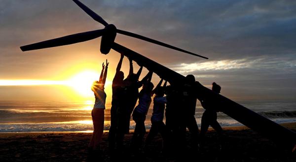 Ein Windrad wird vor einem Sonnenuntergang am Strand aufgestellt.