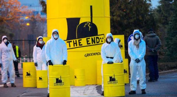 Greenpeace-Aktivisten in weißen Schutzanzügen stehen neben gelben Atommüll-Tonnen mit der Aufschrift "The End" und einem stilisierten AKW