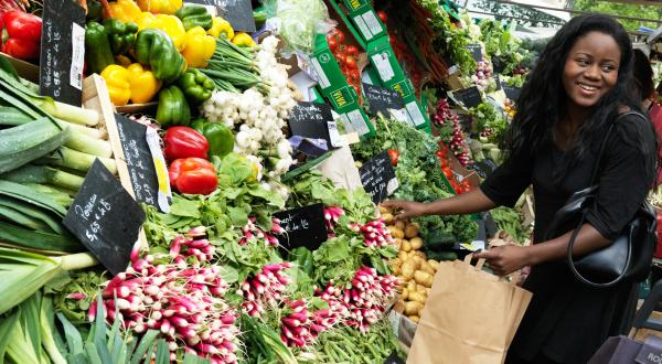 Eine Frau kauft Gemüse an einem Marktstand