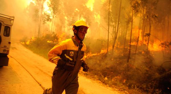 Ein Feuerwehrmann läuft eine Straße entlang; hinter ihm brennt der Wald.