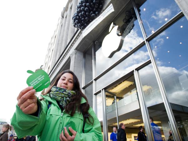 Greenpeace Aktivist:innen verteilen apfelförmige Flugblätter, die auf die schmutzige Energiepolitik von Apple hinweisen, und installieren ein Banner an der Fassade des Apple Stores, das von schwarzen Luftballons getragen wird. Text: "Kein Kohlestrom für die Apple Cloud".