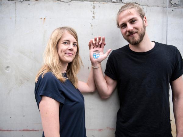 Ein Paar hält sich an der Hand, auf der ein Tattoo zu sehen ist: "Planet Earth First" und ein Herz. 