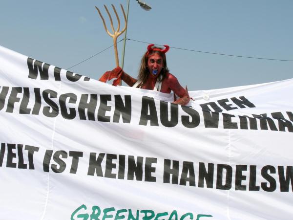 Mann im Teufelskostüm protestiert gegen die WTO. Banner mit der Aufschrift: "Teuflischer Ausverkauf. Umwelt ist keine Handelsware."