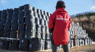 Greenpeace-Mitarbeiterin vor einem Berg mit Plastiksäcken voll radioaktivem Müll.