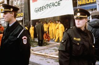 Sechs Kettensägen und Trompeten spielen die kanadische Hymne. Gleichzeitig holzen die Greenpeace-"Holzfäller" vor der kanadischen Botschaft in Wien einen Wald von 16 Fichten ab. Sie fordern die sofortige Freilassung der acht Greenpeace-Kolleg:innen in Vancouver/Kanada und einen Stopp der Abholzung im kanadischen Clayoquot Sound. Ein Transparent an der Botschaft zeigt einen gefällten Ahorn: "Oh Canada". Nach zwei Stunden wird die Aktion von der Polizei gestoppt und 11 Aktivisten werden verhaftet.