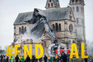 In der Nähe der Abrissmaschinen und der Kirche zeigen die Umweltaktivist:innen ein Schild mit der Aufschrift: "#Endkohle".