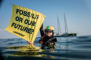 Dänische Aktivistin im Wasser mit einem Banner "Fossils or our future"