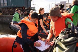 Greenpeace-Bildungsexperte Markus Power und ein Schüler füllen einen Zettel aus sitzend auf einem Schlauchboot