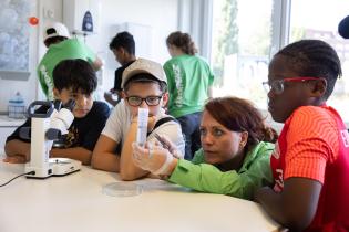 Greenpeace-Konsumexpertin Viola Wohlgemuth untersucht Proben mit drei Schülern im Labor