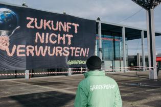 Aktive hängen Banner an Fassade "Zukunft nicht verwursten" steht neben einer Erdkugel, die durch den Fleischwolf gedreht wird.