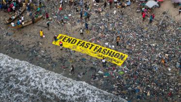 Großes Banner "End Fast Fashion" liegt am Strand in Ghana zwischen Textilmüll.