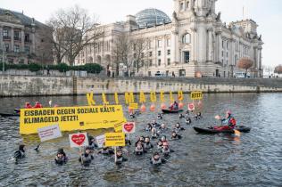 Aktive in Booten und im Wasser der Spree, große Buchstaben auf Schwimmbojen bilden den Schriftzug „Klimageld jetzt!“. Im Hintergrund der Reichstag.