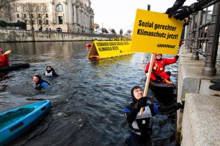 Ein Aktivist im Wasser nimmt ein Schild entgegen "Sozial gerechter Klimaschutz jetzt!"