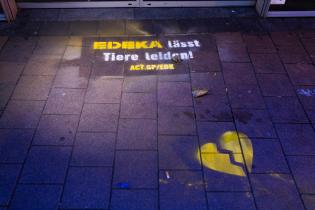 Auf Straßenpflaster gesprühtes gebrochenes, gelbes Herz, daneben der Schriftzug: Edeka lässt Tiere leiden