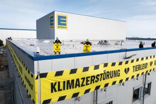 Vom Dach des Edeka-Werkes hängen fünf lange Banner in Absperrband-Optik mit der Warnung: “Tierleid und Klimazerstörung”.