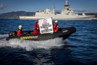 Aktivist:innen von Greenpeace Italien an Bord des Schiffes Rainbow Warrior prangern Militärmissionen zum Schutz fossiler Brennstoffe an. Auf Transparenten: "Verteidigt das Klima, nicht die fossilen Brennstoffe".