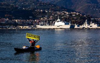 Aktivist:innen von Greenpeace Italien an Bord des Schiffes Rainbow Warrior prangern Militärmissionen zum Schutz fossiler Brennstoffe an. Auf Transparenten: "Verteidigt das Klima, nicht die fossilen Brennstoffe".