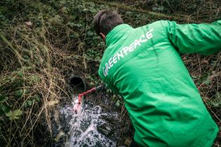 Aktivist nimmt Wasserproben aus einem Abwasserrohr