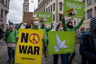 Der Ostermarsch beginnt am Moritzplatz in Augsburg, an dem auch Greenpeace Freiwillige teilnehmen. Sie halten Banner und Schilder mit Friedenszeichen und den Forderungen "Kein Krieg" und "Frieden" hoch.