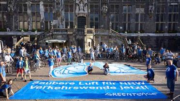 Aktivisten legen zwei Banner vor das Aachener Rathaus: eines zeigt eine blaue Lunge als Symbol für schlechte Luft durch Stickoxide, auf dem zweiten Banner steht "Saubere Luft für NRW. Verkehrswende jetzt!"