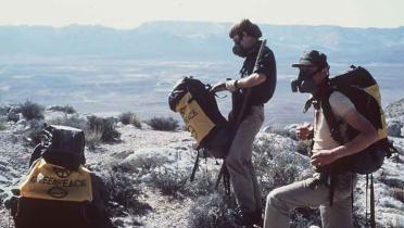 Greenpeace-Aktivisten sind mit Rucksäcken und Atemschutzmasken auf einem Atomwaffentestgelände in Nevada, Juli 1983