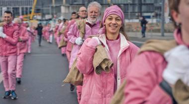 Zwei Reihen rosa gekleideter Menschen laufen mit Kohlesäcken durch Berlin