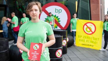 Vor der Europazentrale des Ölkonzerns BP in der Hamburger Hafencity halten Aktivistinnen und Aktivisten ein Banner "BP zerstört das Klima", an der Glasfassade klebt ein durchgestrichenes BP-Logo, vor dem Eingang liegen Ölfässer.