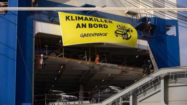 Greenpeace-Aktivisten und Aktivistinnen protestieren in Bremerhaven an einem Transportschiff, das mehrere 100 weitere BMW-Sportgeländewagen nach Deutschland liefert. An der Schiffswand haben sie ein Banner mit dem Slogan „Klimakiller an Bord“ angebracht.