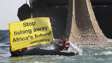Zwei Greenpeace-Aktivisten auf einem Schlauchboot protestieren vor einem Schlepper gegen Industriefischerei um Afika