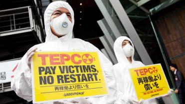 Zwei Greenpeace-Aktivisten in weißen Overalls und mit weißen Atemmasken halten gelbe Schilder mit der Aufschrift: Tepco: Pay Victims, no restart.