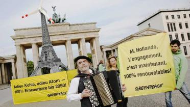 Greenpeace-Aktivisten und ein Akkordeonspieler protestieren vorm Brandenburger Tor für die Energiewende. Dort haben sie eine Eiffelturm-Attrappe mit Windrad obendrauf aufgebaut.