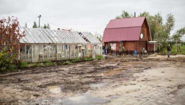 Ein Wohnhaus im autonomen Kreis der Chanten und Mansen, danebenein Gewächshaus. Vor den beiden Häusern liegt ein schlammiges Grundstück voller Pfützen