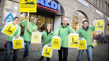 Fünf Greenpeace-Aktivisten vor einer Aldi-Filiale. Sie halten ein Plakat und Kanister mit der Aufschrift "Pestizide schaden der Artenvielfalt".
