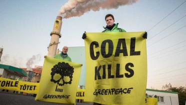 Greenpeace-Aktivisten stehen vor dem Schlot des Kohlekraftwerks Deuben. Sie halten Banner mit einem Totenkopf und mit der Aufschrift Coal Kills.